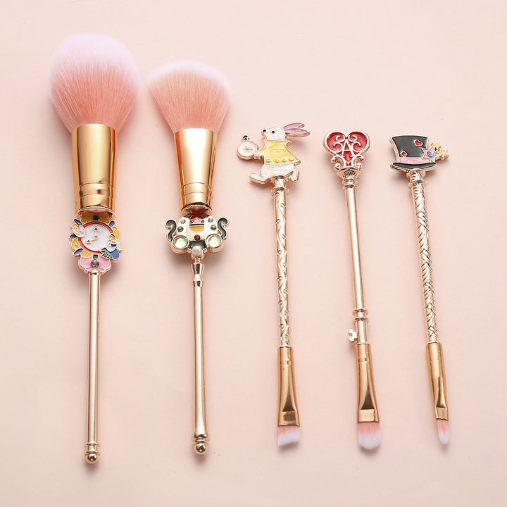 Decorative makeup brushes with whimsical fairy tale-inspired designs on a pale pink surface.